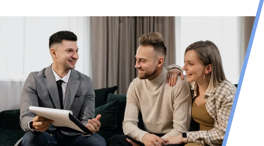 An image with a male realtor showing a paper to a couple sitting on a sofa.