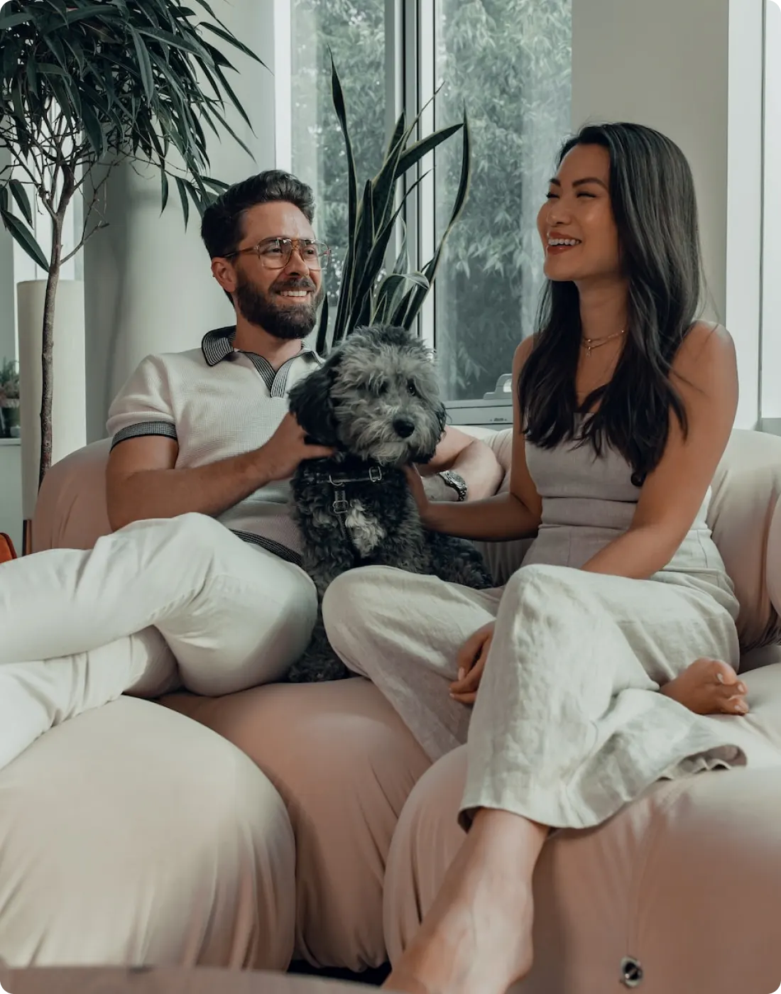 A picture of a happy couple sitting on a sofa with a dog between them.