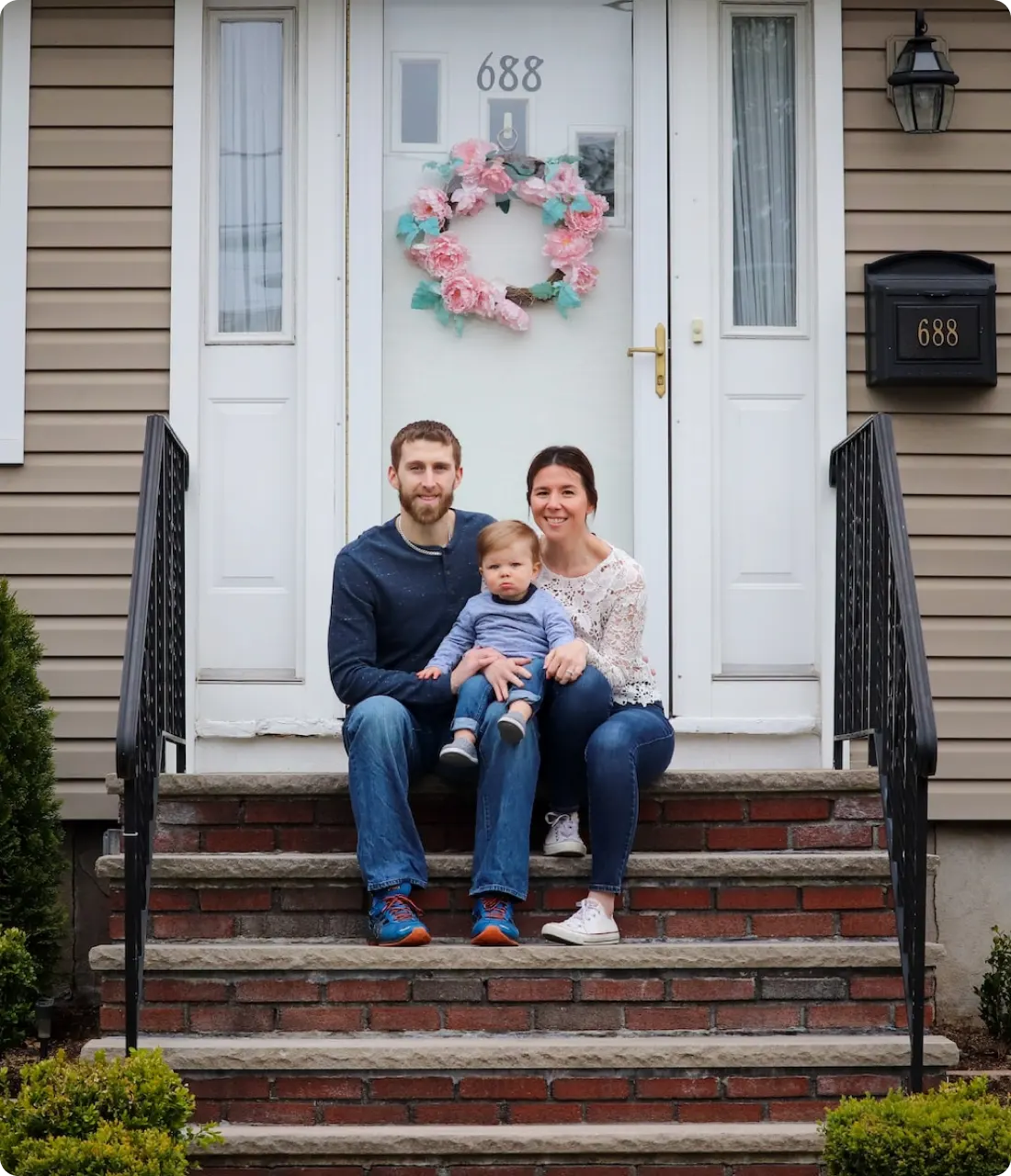 An image of a couple with their son sitting on a stair in front the main door of their house.